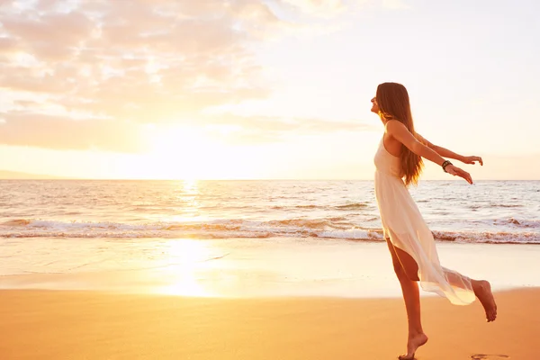 Glückliche unbeschwerte Frau, die bei Sonnenuntergang am Strand tanzt — Stockfoto
