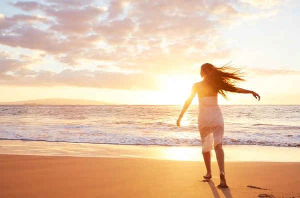 Glückliche unbeschwerte Frau, die bei Sonnenuntergang am Strand tanzt — Stockfoto