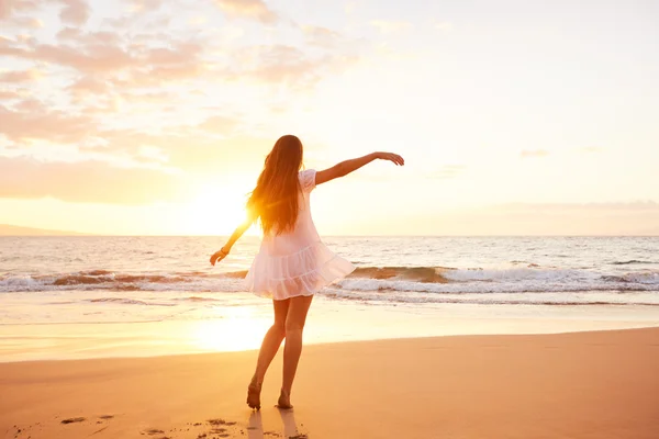 Glückliche unbeschwerte Frau, die bei Sonnenuntergang am Strand tanzt — Stockfoto