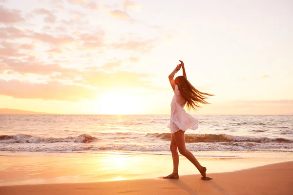 Glückliche unbeschwerte Frau, die bei Sonnenuntergang am Strand tanzt — Stockfoto