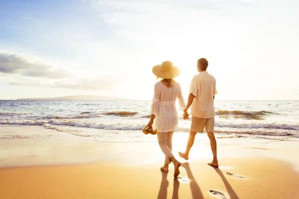 Älteres Paar spaziert bei Sonnenuntergang am Strand Stockbild