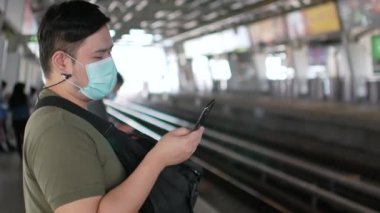 Maske takan bir adamın POV 'u Corona virüsünden korunurken Covid19 cep telefonu kullanarak yaklaşan hava trenini bekliyor.