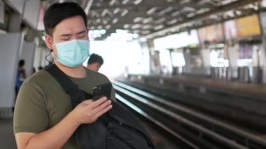 Maske takan bir adamın POV 'u Corona virüsünden korunurken Covid19 cep telefonu kullanarak yaklaşan hava trenini bekliyor.