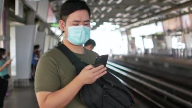 Maske takan bir adamın POV 'u Corona virüsünden korunurken Covid19 cep telefonu kullanarak yaklaşan hava trenini bekliyor.