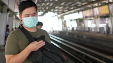 Maske takan bir adamın POV 'u Corona virüsünden korunurken Covid19 cep telefonu kullanarak yaklaşan hava trenini bekliyor.
