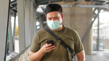 Maske takan bir adamın POV 'u Corona virüsünden korunurken Covid19 cep telefonu kullanarak yaklaşan hava trenini bekliyor.