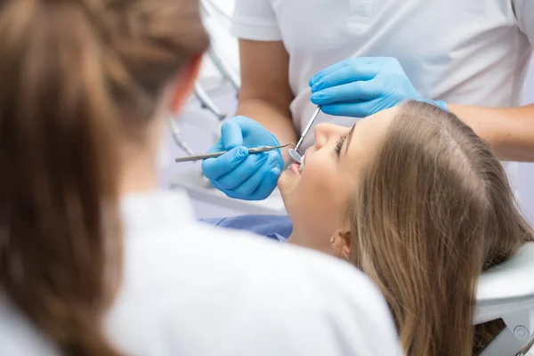 Docteur En Gants Médicaux Noirs Examine Les Dents De La Jeune Fille En  Utilisant Un Microscope Dentaire Et Un Miroir Dans Le Bureau Du Dentiste.  La Femme A Un Bavoir Du Patient