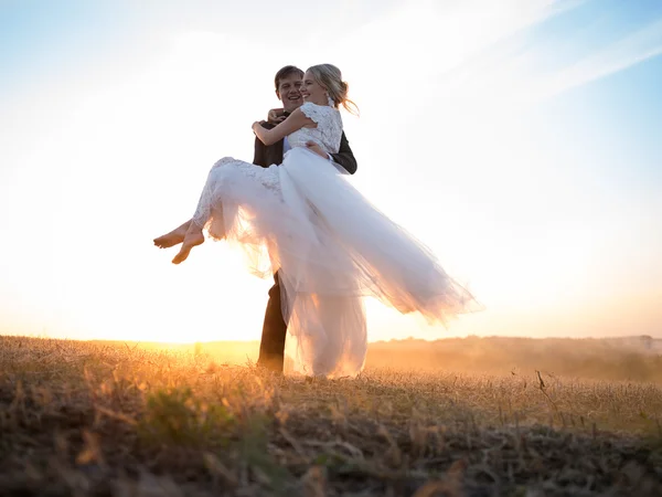 Ehemann trägt seine geliebte Frau im Arm, in der untergehenden Sonne — Stockfoto