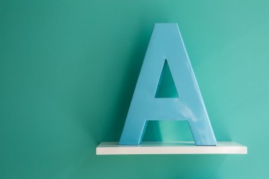 Letter A turquoise color on a white shelf.