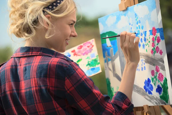 Vacker blond kvinna konstnär målar en färgglad bild. — Stockfoto