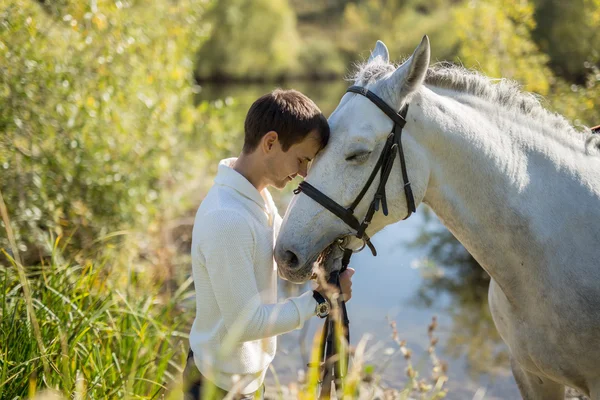 Homem fica perto do lago com um cavalo — Fotografia de Stock