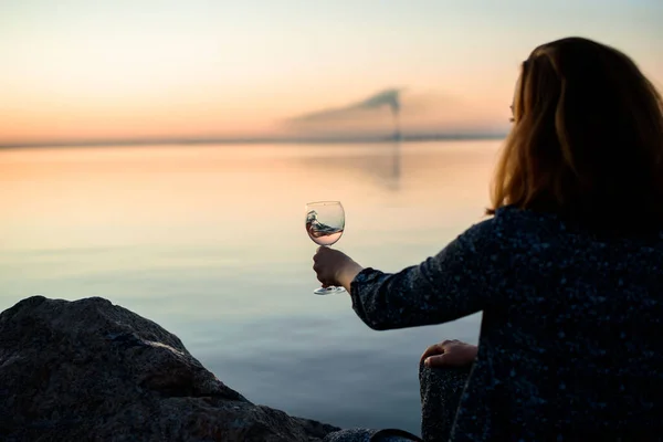 A beautiful glass with pink wine in the hands of a young girl. A glass of wine at sunrise. Romantic breakfast by the sea and sun