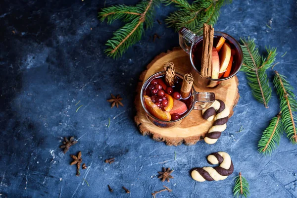 İki bardak portakal, karanfil, tarçın ve anason süslemeli sıcak kırmızı şarap. Arka planda Noel ışıkları. Kırsal dekor, rahat atmosfer, şenlik havası. Aile zamanı, yeni yıl arifesi