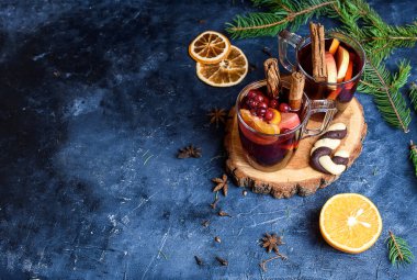 İki bardak portakal, karanfil, tarçın ve anason süslemeli sıcak kırmızı şarap. Arka planda Noel ışıkları. Kırsal dekor, rahat atmosfer, şenlik havası. Aile zamanı, yeni yıl arifesi