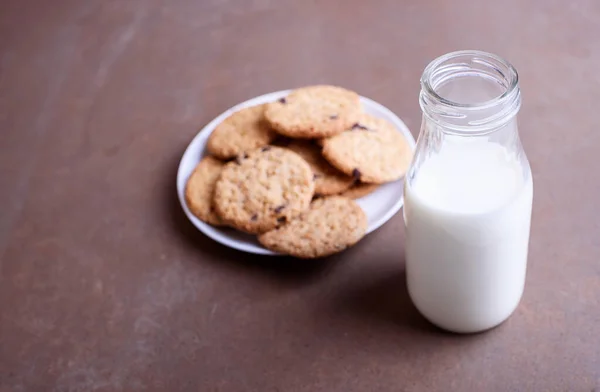 Fresh delicious milk in a glass bottle on a textured background with chocolate cookies on a white plate. A place for text.