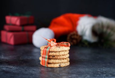 Çikolatalı lezzetli kurabiyeler, kırmızı kurdele, ladin filizi, Noel Baba şapkası, koyu arkaplanlı kısa boylu..