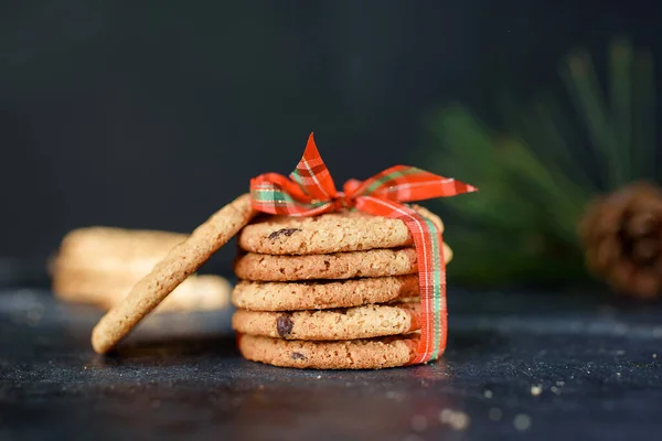 Läckra småbröd kakor med bitar av choklad, med rött band, en kvist gran, tomte hatt, en shortie på en mörk bakgrund. — Stockfoto