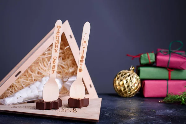 A wooden box gift with a marshmallows for coffee and spoons with chocolates in the form of a star Christmas tree. New Years content.