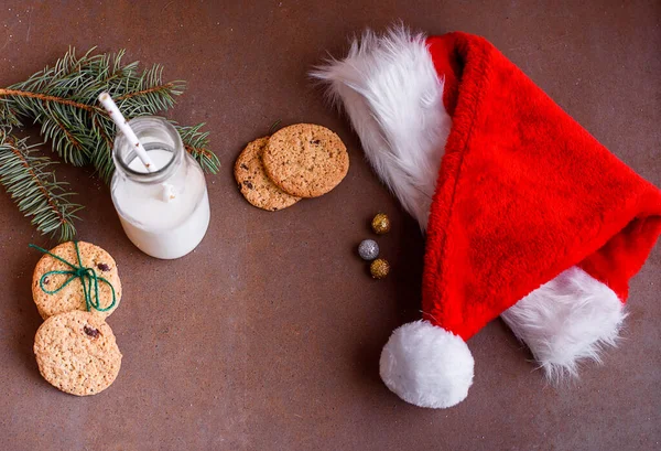 New Year\'s content with baked cookies, milk, gifts, toy for the Christmas tree, Christmas tree twigs, view from above. Place for text. Holidays content with santas hat