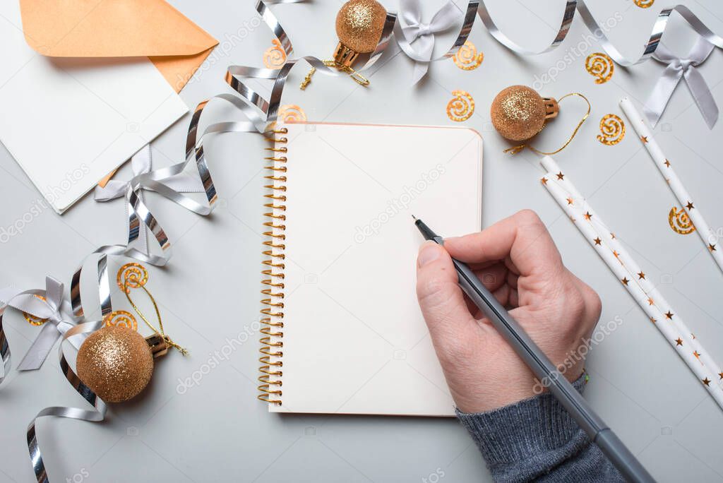 Happy New Year 2021. Woman's hand writing in notebook decorated with Christmas decorations on the grey background. Top view, flat lay. New years concept