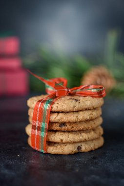 İçinde çikolata parçacıkları olan kurabiyeler koyu arkaplanda kırmızı güzel bir kurdele ile bağlanır. Mesajlaşmak için bir yer. Yukarıdan bak. Yeni yıl kurabiyeleri
