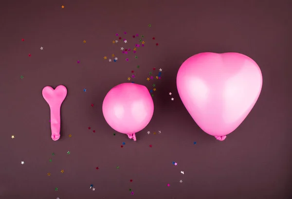 Three pink balloons for helium and air in the shape of a heart of different sizes on a brown background with vomit. Art , holidays concept