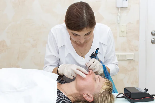 Lip tattoo and correction of the shape of a middle-aged woman in a beauty salon.