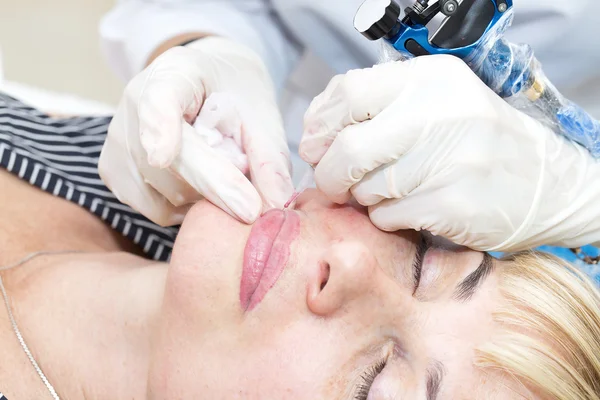 Lip tattoo and correction of the shape of a middle-aged woman in a beauty salon.