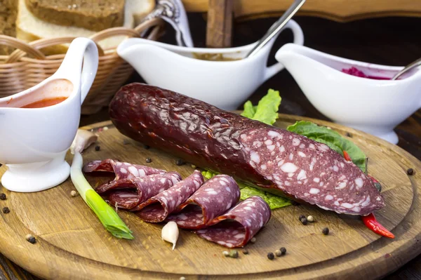 Sausages on a wooden plate with vegetables — Stock Photo, Image