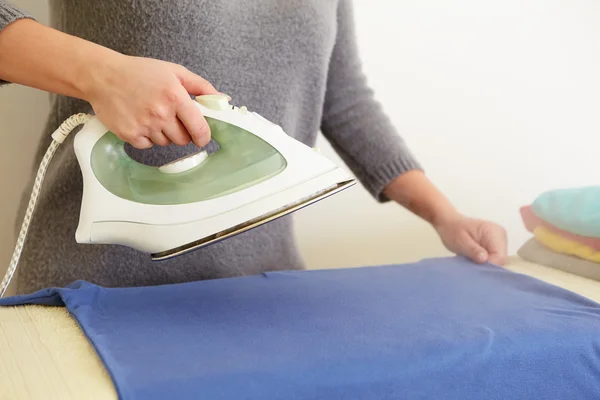 Woman ironing blue polo shirt — Stock Photo, Image