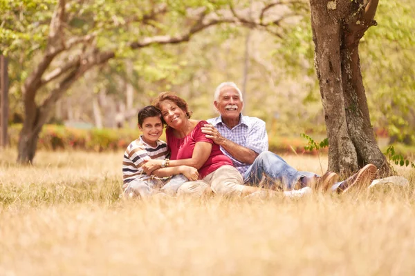 Senior paar grootouders knuffelen jongen op gras — Stockfoto