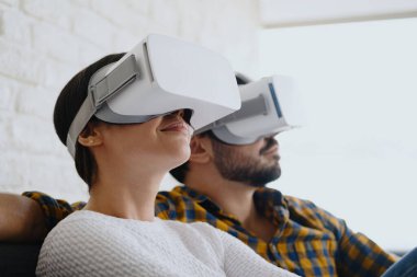 Genç çift koltukta kulaklıkla sanal gerçeklik oynuyorlar.