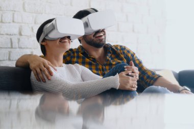 Genç çift koltukta kulaklıkla sanal gerçeklik oynuyorlar.