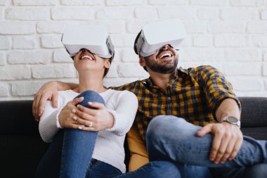 Genç çift koltukta kulaklıkla sanal gerçeklik oynuyorlar.