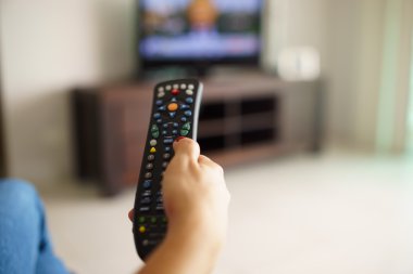 Uzaktan kumandayla kanal değiştirme tv izlerken oturan kadın