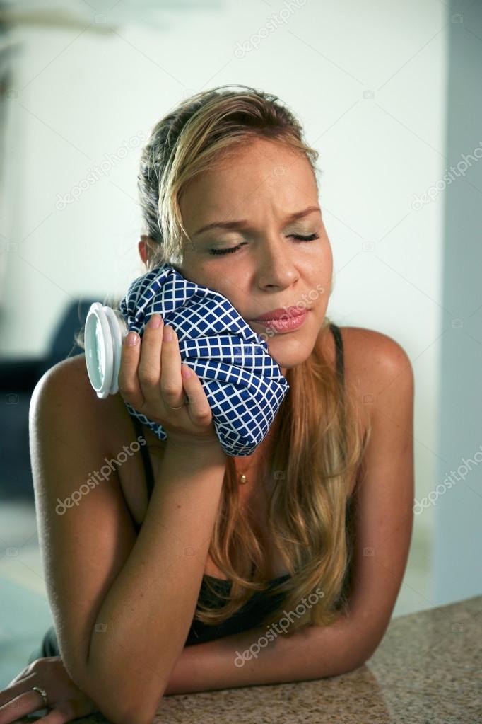 Young woman with toothache holding ice bag on mouth