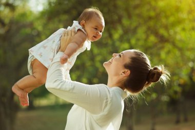 Anne yukarı kaldırarak ve çevresinde küçük bebek kızı par Torna