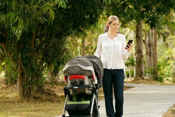 Madre con el bebé en la silla de paseo escribiendo mensaje en el teléfono —  Fotos de Stock