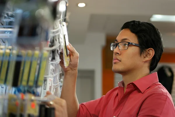 Hombre chino ordenando unidad USB en el estante en la tienda de computadoras —  Fotos de Stock