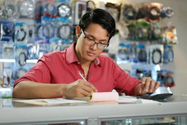 Chinese Man Working In Computer Shop Checking Bills And Taxes clipart