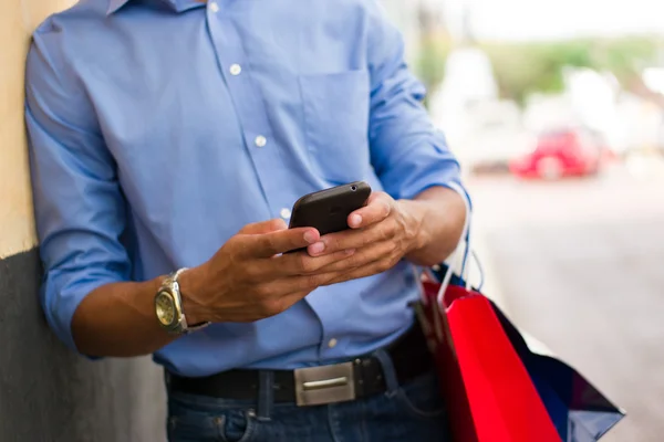 Homem afro-americano digitando mensagem no telefone sacos de compras — Fotografia de Stock