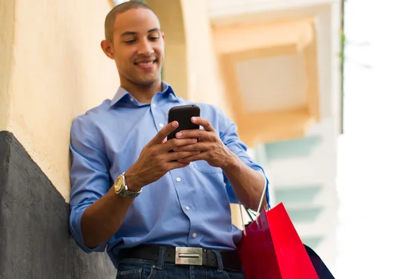 African American Man textmeddelanden på telefonen med kassar och påsar — Stockfoto