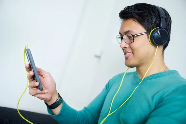 Cinese uomo con verde cuffie ascolta podcast telefono a casa — Foto Stock