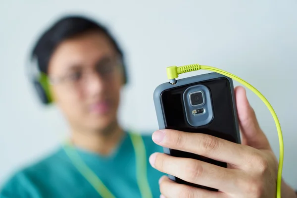 Homem chinês com fones de ouvido verdes ouve música Podcast telefone — Fotografia de Stock