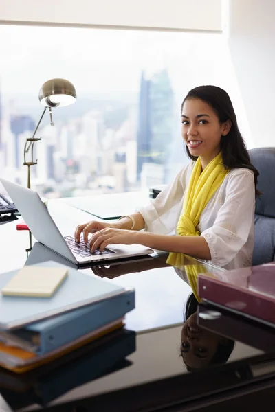 Assistente donna d'affari sorride alla macchina fotografica digitando su PC — Foto Stock