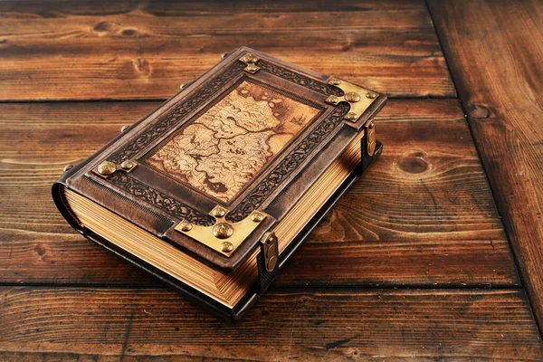 Üzerinde eski dünya haritası olan kahverengi deri kitap, yaldızlı kağıt kenarlar ve kayışlar, eskimiş ahşap masaya uzan. 