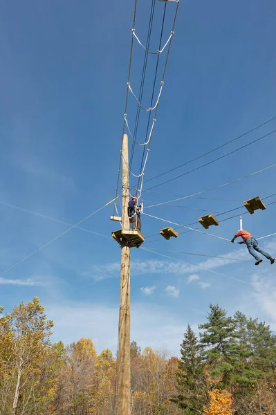 Ropes course/challenge course.  Wide-angle photo of participant walking across guide wire.