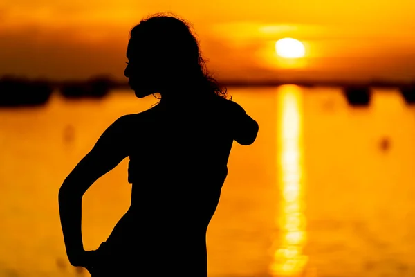 A beautiful latin model is silhouetted as she poses with the rising sun behind her on a exotic Caribbean beach