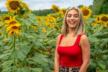 Sarışın bir model, yaz gününün tadını çıkarırken ayçiçeği tarlasında poz veriyor.