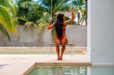 A beautiful brunette bikini model swings by the pool in the Yucatan Peninsula near Merida, Mexico